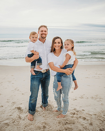 Zach and wife tnad on beach holding their son and daughter